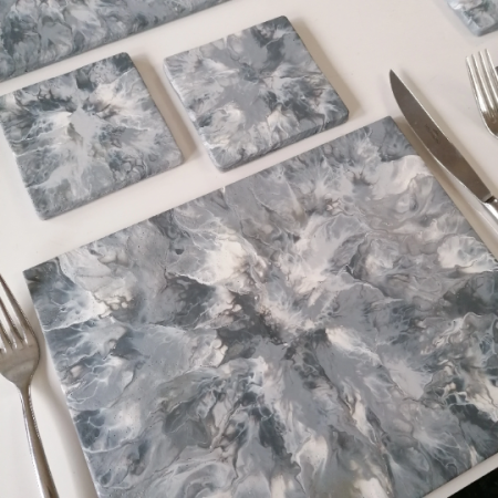 Unique modern grey placemats and coasters. Hand painted with light grey, charcoal, white and metallic silver in an abstract art style with splashes of the colours covering the entire rectangular placemats and square coasters. These are hand painted tiles, each one is different and yet they all match for a set.