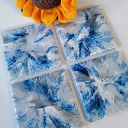 Navy blue ceramic tile coasters hand painted in an abstract manner with navy blue, light grey, white and metallic silver acrylic paint. Coasters measure 10cm by 10cm, are varnished to make them heat resistant and wipeable, plus cork added to the underside to protect furniture.