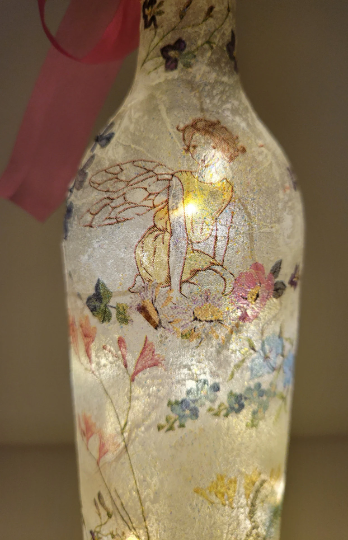 Lit up standard wine bottle with Fairy and flower butterfly detailing. Pink organza ribbon tied around the neck of the bottle. Cork LED lights