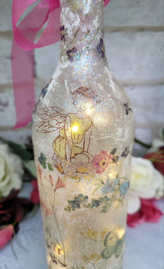 Lit up standard wine bottle with Fairy and flower butterfly detailing. Pink organza ribbon tied around the neck of the bottle. Cork LED lights