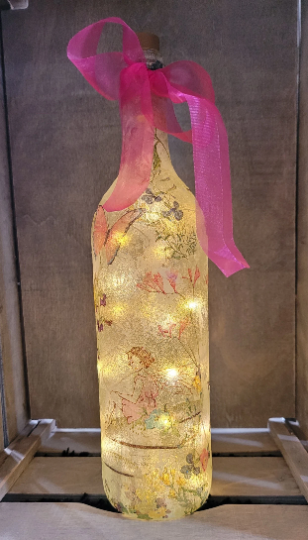 Lit up standard wine bottle with Fairy and flower butterfly detailing. Pink organza ribbon tied around the neck of the bottle. Cork LED lights