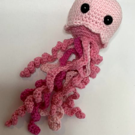 Acrocheted jellyfish with a light pink body and darker pink tentacles below.