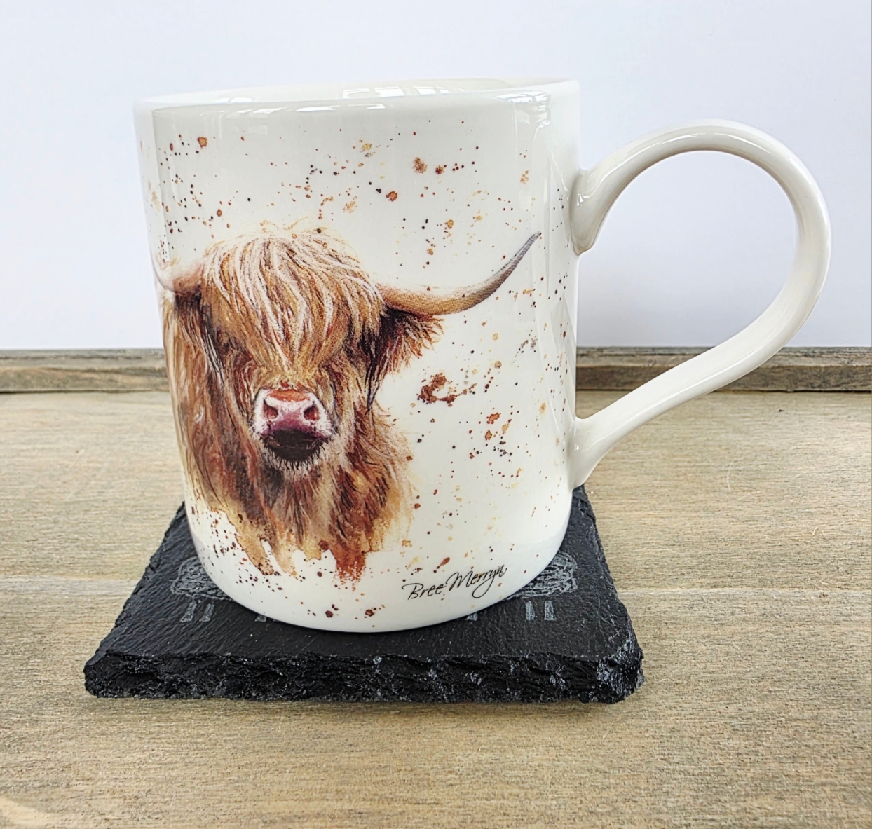 Mug with a highland cow design on a black slate coaster on a wooden surface