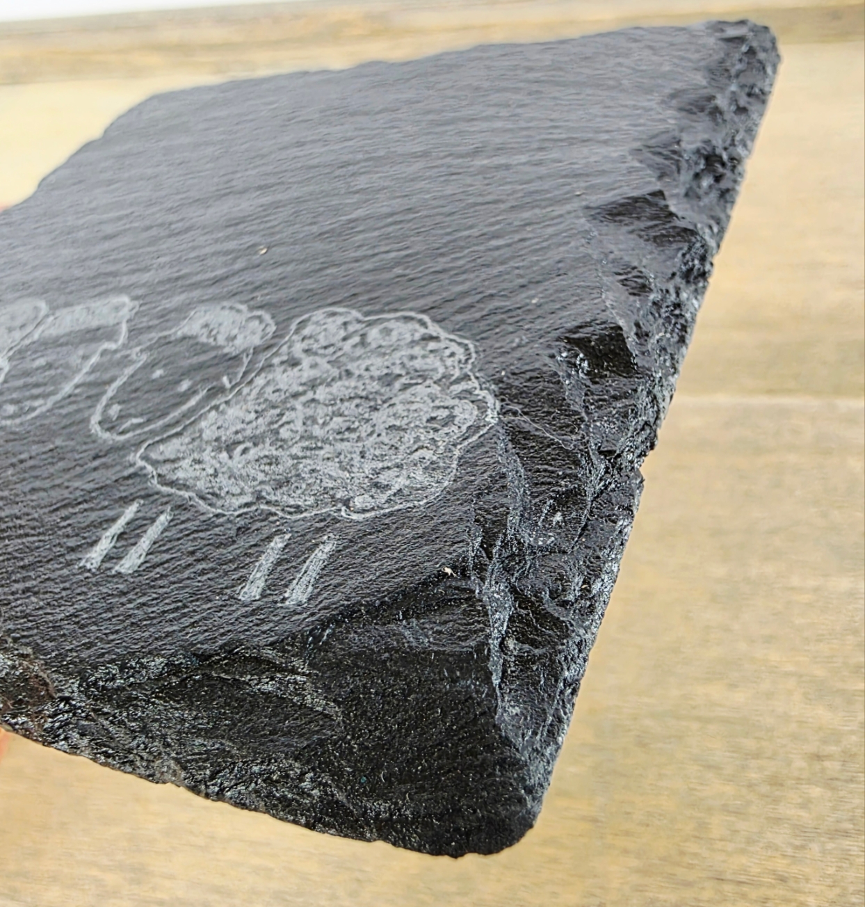 Slate coaster with engraved sheep design on a wooden surface