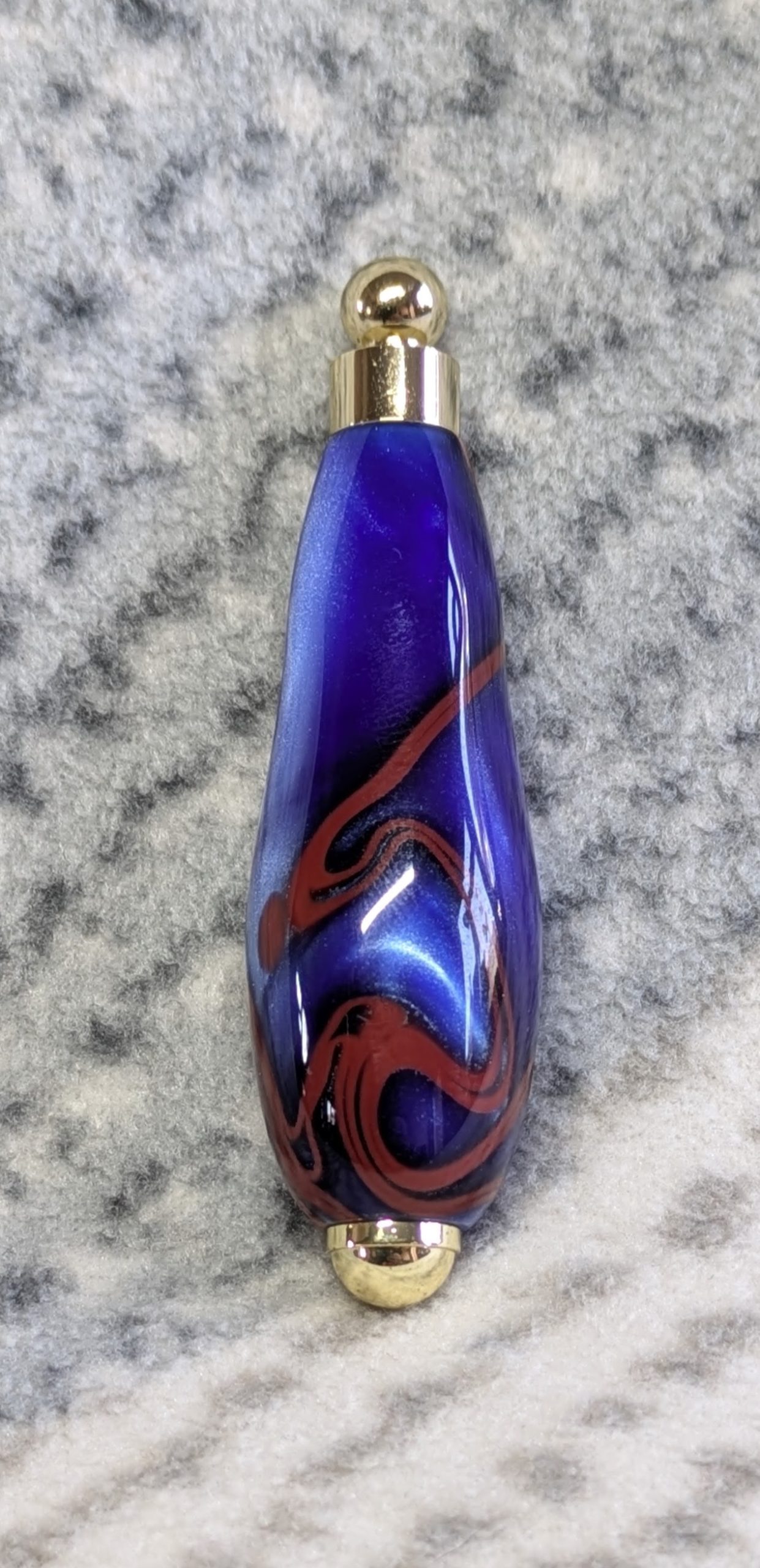 Light switch pull pendant made from blue acrylic with red swirls and gold coloured fittings