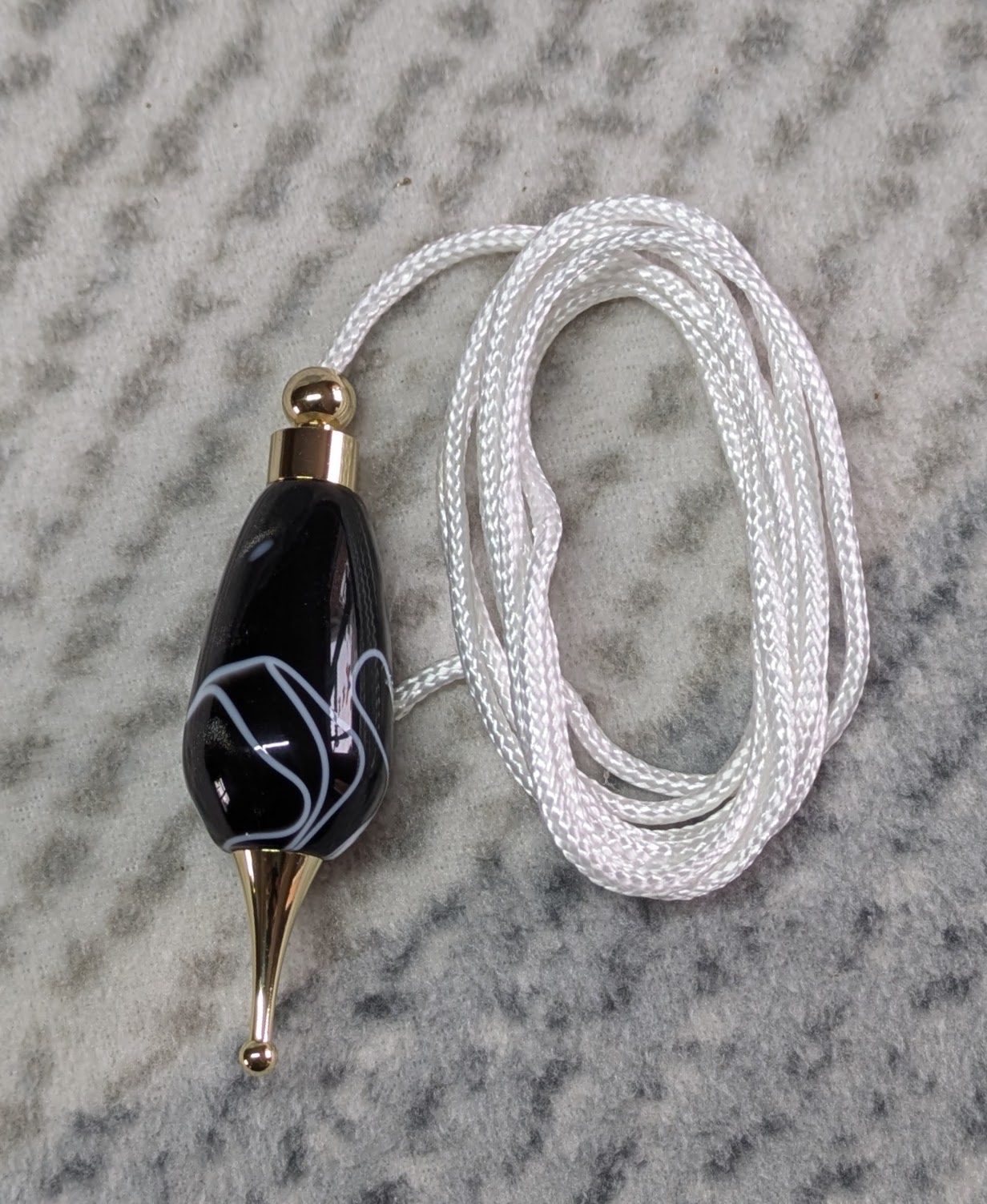 Light switch pull pendant made from black acrylic with white swirls and gold coloured fittings