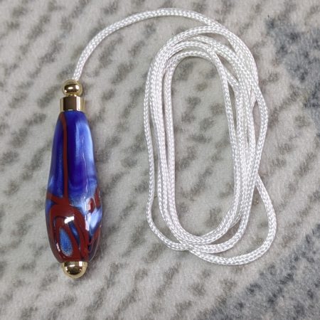 Light switch pull pendant made from blue acrylic with red swirls and gold coloured fittings