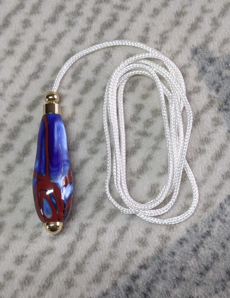 Light switch pull pendant made from blue acrylic with red swirls and gold coloured fittings