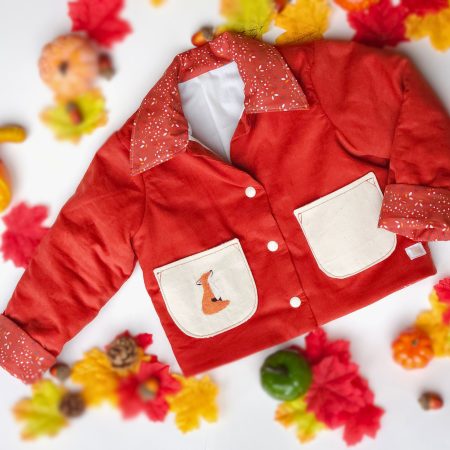 Rust toddler corduroy jacket with cream pockets, confetti fabric collar and cuffs, and a hand-embroidered fox, styled with autumn leaves and pumpkins.