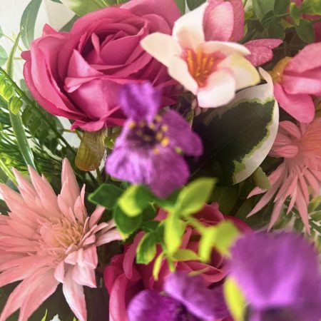 A cheerful wreath with pink and purple flowers on a natural grapevine base H60cm x W50cm