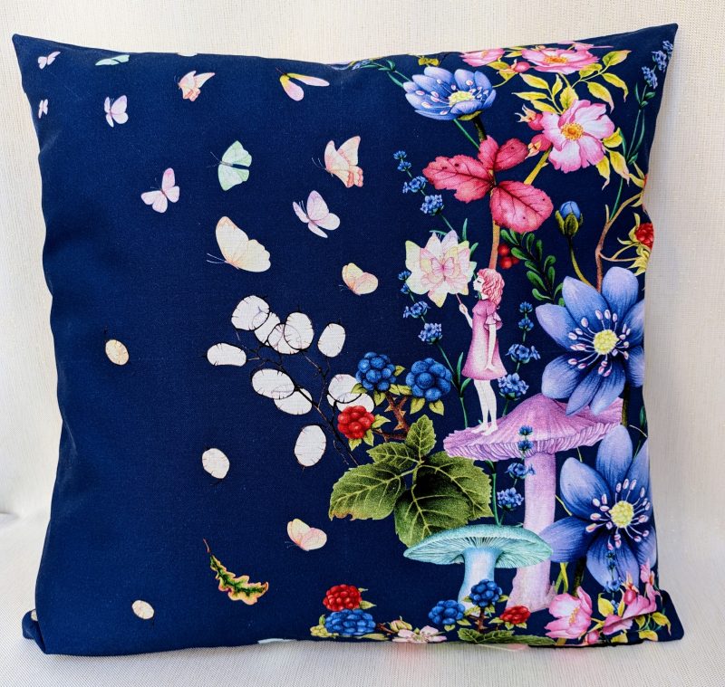 Decorative cushion cover showing a girl standing on a mushroom holding a butterfly surrounded by flowers and floating butterflies on a navy background.