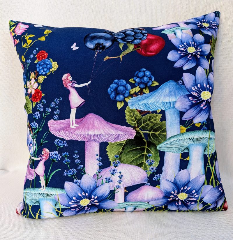 Illustrated cushion cover featuring a girl standing on a mushroom holding berry shaped balloons surrounded by flowers and butterflies on a navy background.