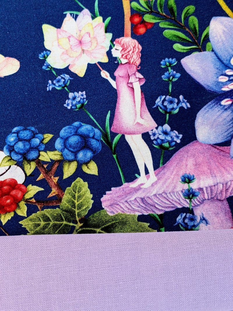 Detail showing the lining for the decorative cushion cover showing a girl standing on a mushroom holding a butterfly surrounded by flowers and floating butterflies on a navy background.