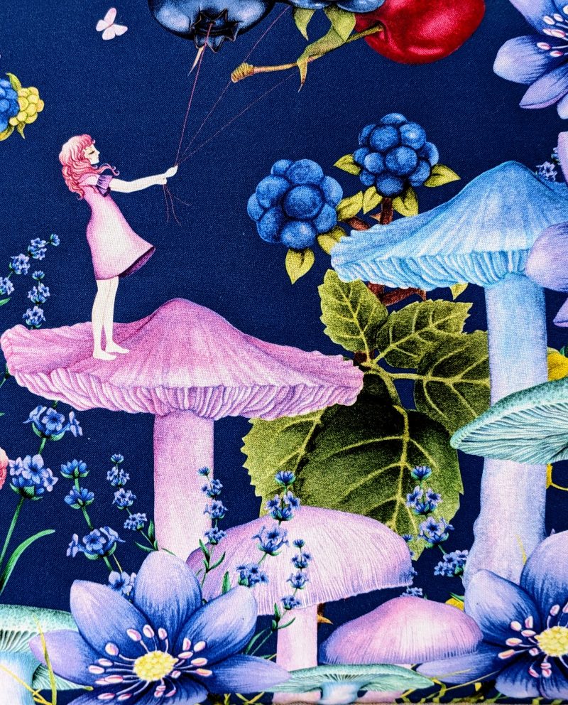 Close up of detail of the illustrated cushion cover featuring a girl standing on a mushroom holding berry shaped balloons surrounded by flowers and butterflies on a navy background.