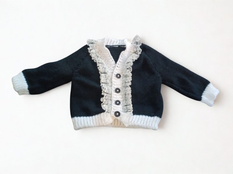 Long sleeved black cardigan with white trim. A lovely lace trim up the front and around the neck can be added. Comes is various sizes. Acrylic yarn for easy care.
