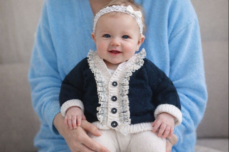 Long sleeved black cardigan with white trim. A lovely lace trim up the front and around the neck can be added. Comes is various sizes. Acrylic yarn for easy care.