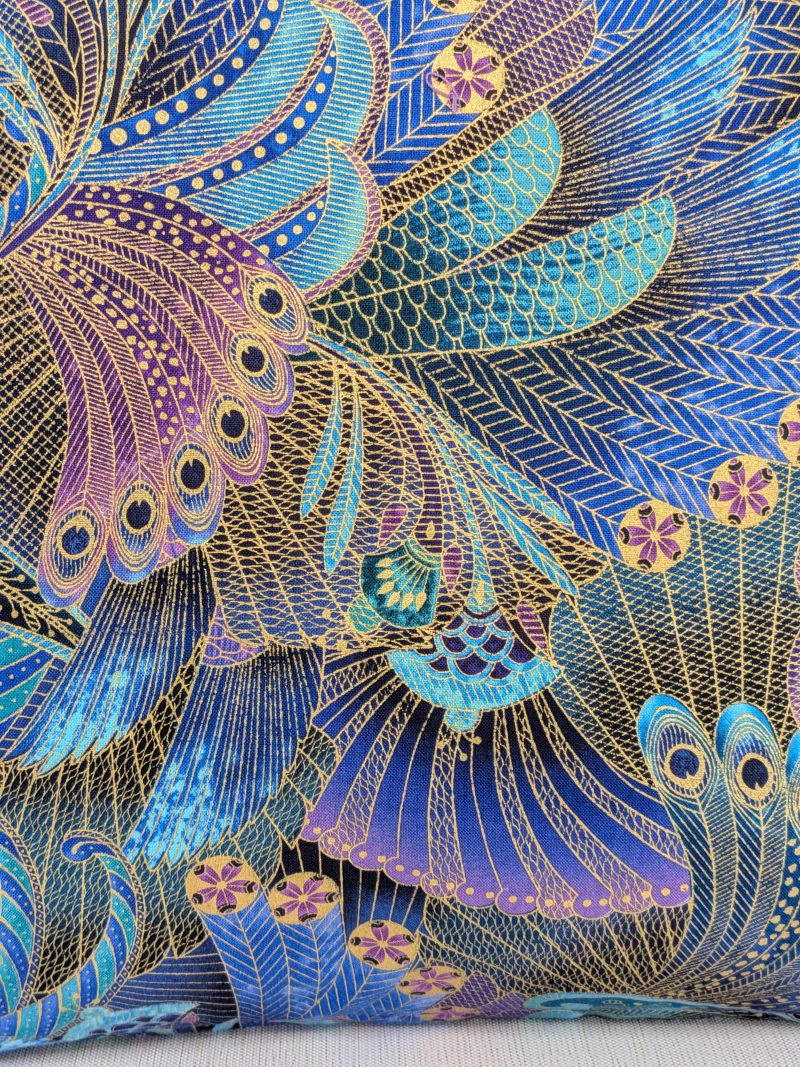 Detail of front of decorative cushion cover with intricate peacock feather pattern in blue, purple, and gold on black background, 18 inch, zipped and lined