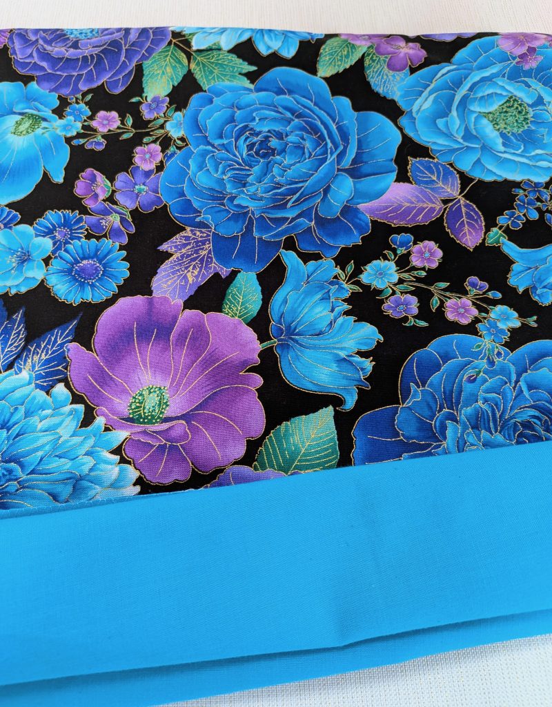 Lining detail of decorative throw pillow cover with vibrant blue and purple floral pattern on a black background, featuring detailed blossoms and leaves.