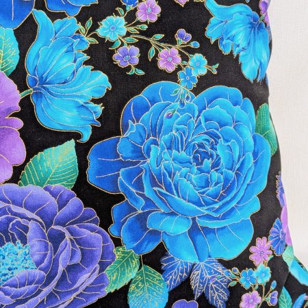 Reverse detail of Reverse detail of decorative throw pillow cover with vibrant blue and purple floral pattern on a black background, featuring detailed blossoms and leaves.