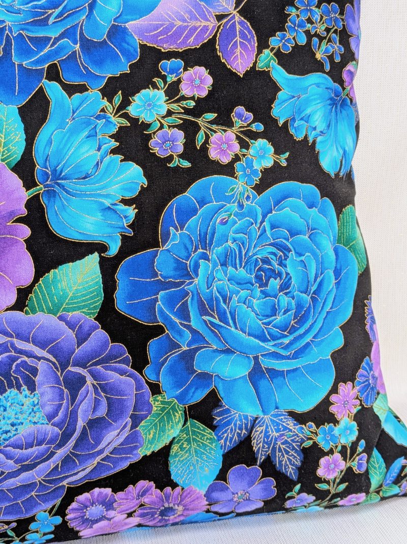 Reverse detail of Reverse detail of decorative throw pillow cover with vibrant blue and purple floral pattern on a black background, featuring detailed blossoms and leaves.