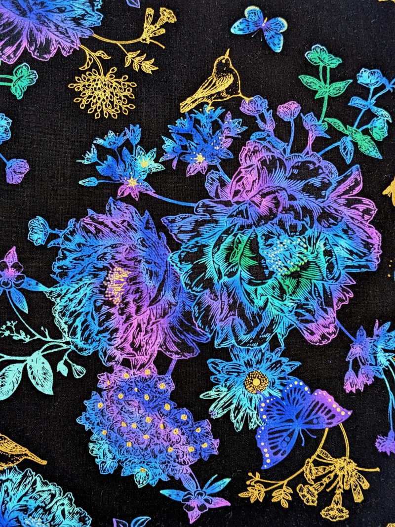 Front detail of black cushion cover featuring colourful rainbow floral pattern with butterflies and gold accents, lined with a zip closure