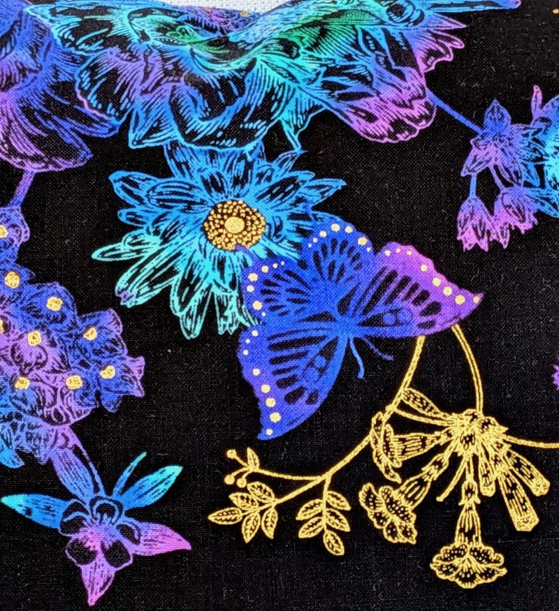 Detail of reverse of black cushion cover featuring colourful rainbow floral pattern with butterflies and gold accents, lined with a zip closure