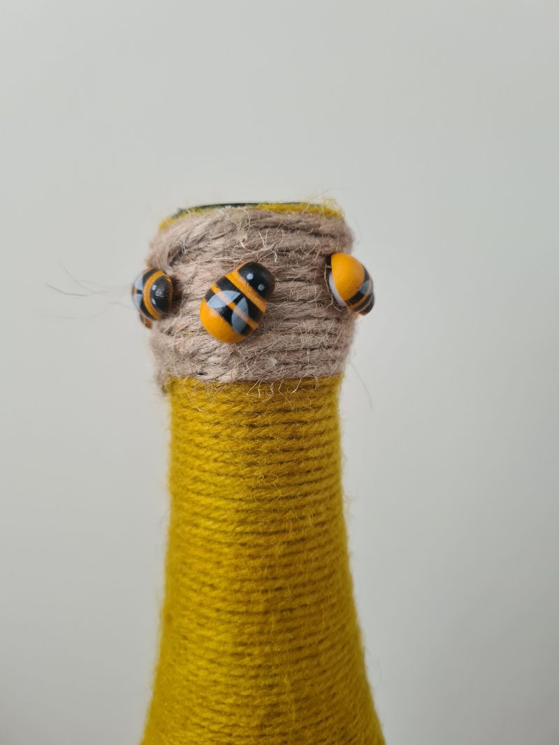 Upcycled wine bottle wrapped with yellow & black yarn with bumble bee decor
