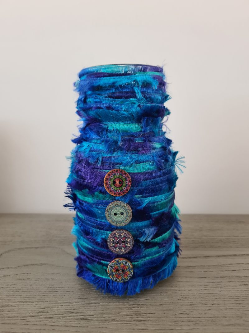 Upcycled glass jar wrapped with blue yarn and decorated with wooden buttons
