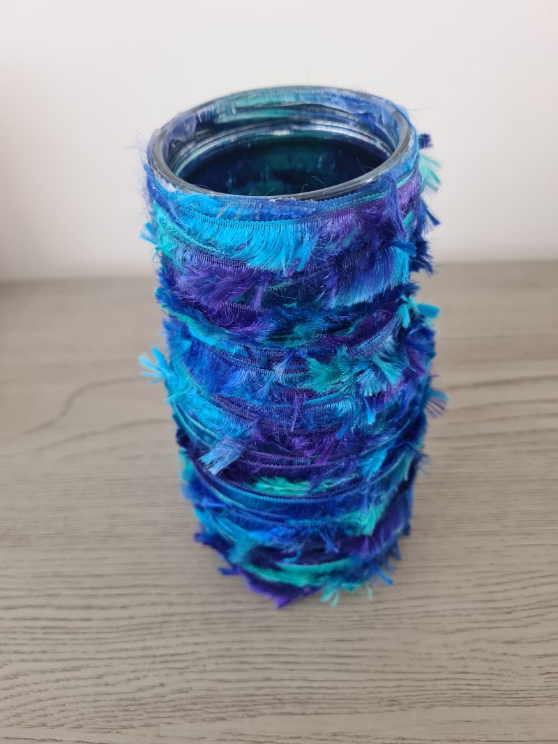 Upcycled glass jar wrapped with blue yarn and decorated with wooden buttons
