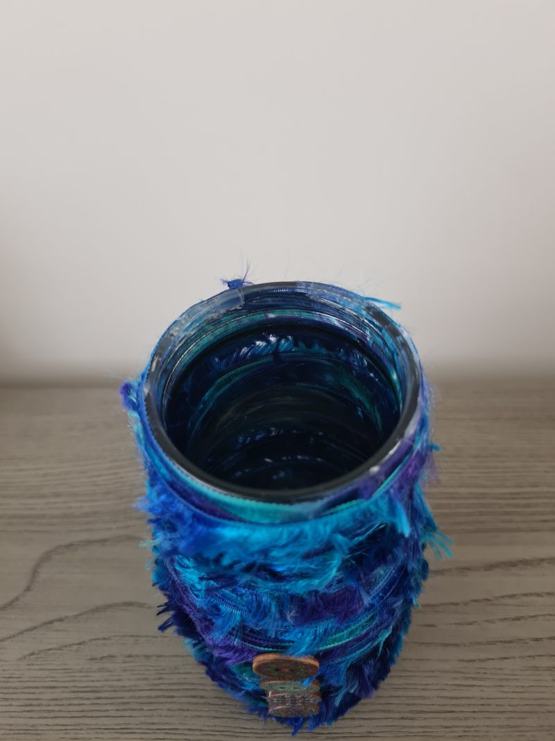 Upcycled glass jar wrapped with blue yarn and decorated with wooden buttons