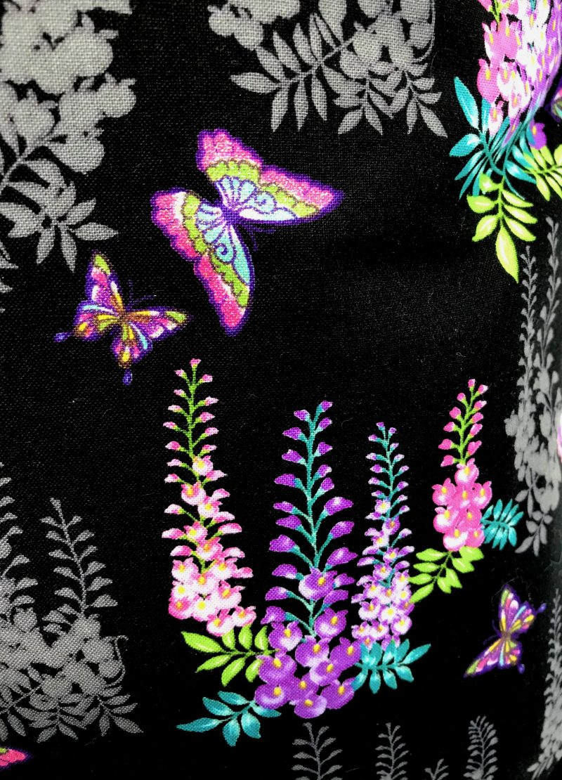 Front detail of black cushion cover with bright pink and purple floral pattern and butterflies, 18 inch square, lined with zip fastening