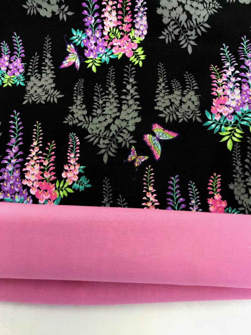Lining detail of black cushion cover with bright pink and purple floral pattern and butterflies, 18 inch square, lined with zip fastening