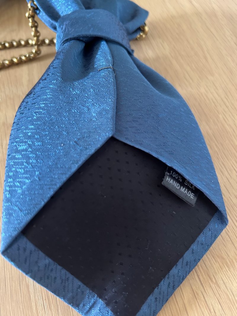 Handmade, elegant blue necktie accessory adorned by a beautiful golden flower brooch.