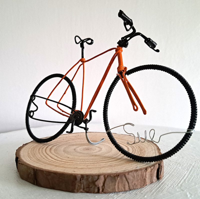Handmade, orange colour, road style wire bicycle sculpture. Approximately 9cm long 4.5cm high, personalised with a name written in wire and set into the front wheel.