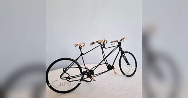 Black miniature tandem sculpture made from galvanised steel and hand painted black with gold handles, seat and pedals. Made as a wedding cake topper and personalised with two names written in wire and set into the front and back wheel of the bicycle.