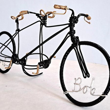 Black miniature tandem sculpture made from galvanised steel and hand painted black with gold handles, seat and pedals. Made as a wedding cake topper and personalised with two names written in wire and set into the front and back wheel of the bicycle