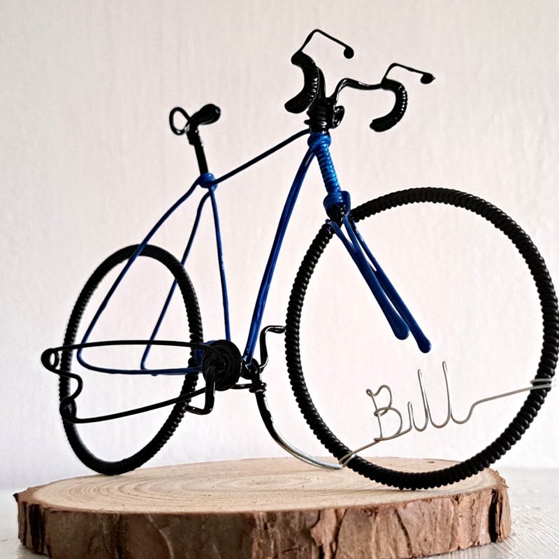 Handmade, blue colour, curved handle bars wire bicycle sculpture. Approximately 9cm long 4.5cm high, personalised with a name written in wire and set into the front wheel.