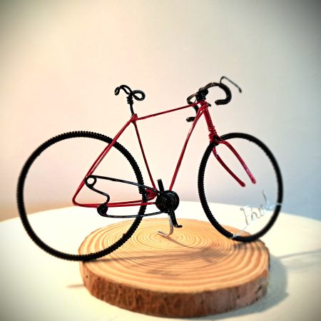 Handmade, red colour, curved handle bars wire bicycle sculpture. Approximately 9cm long 4.5cm high, personalised with a name written in wire and set into the front wheel.