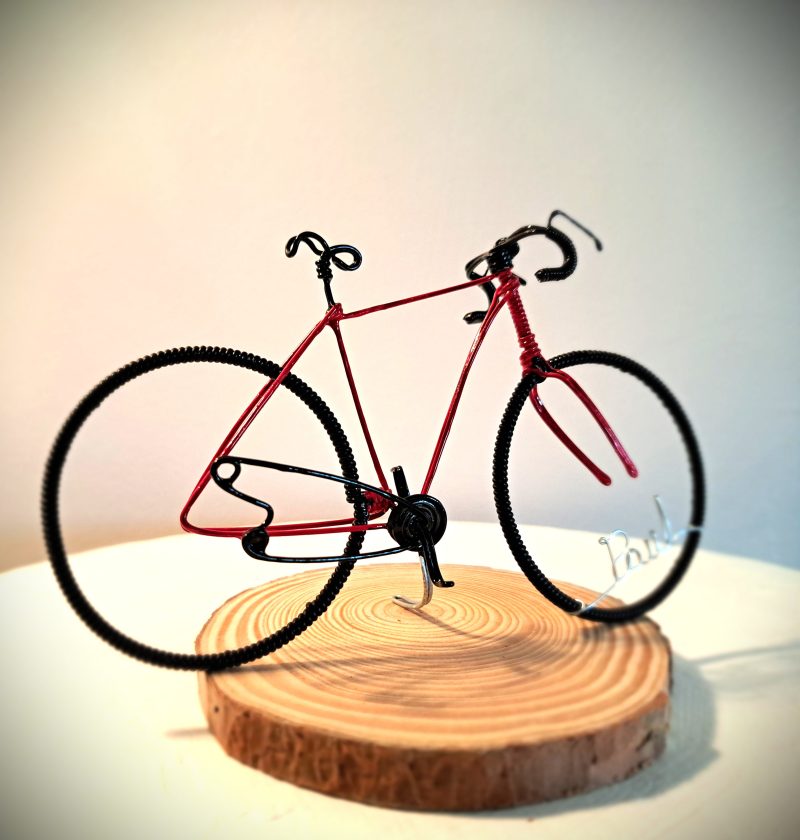 Handmade, red colour, curved handle bars wire bicycle sculpture. Approximately 9cm long 4.5cm high, personalised with a name written in wire and set into the front wheel.