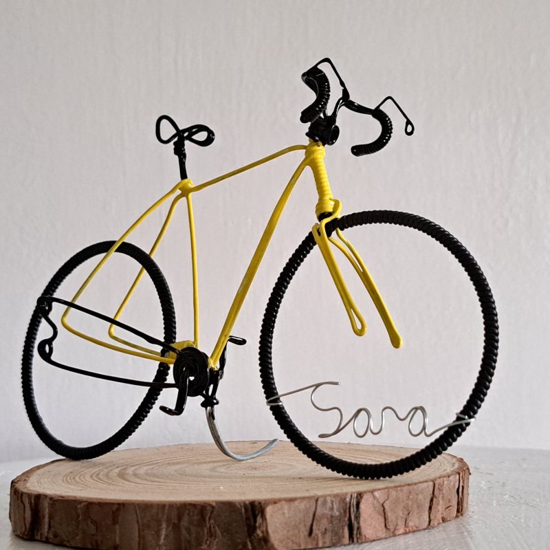 Handmade, yellow colour, curved handle bars wire bicycle sculpture. Approximately 9cm long 4.5cm high, personalised with a name written in wire and set into the front wheel.