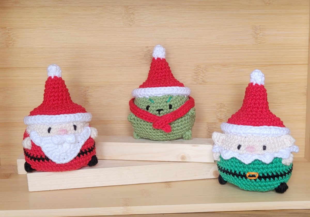 Three crocheted Christmas characters in red hats on a wooden shelf