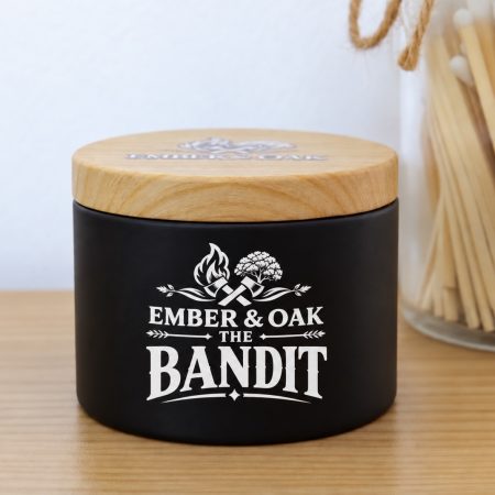 The Bandit candle by Ember & Oak in a black jar with its wooden lid on, standing on a wooden surface.