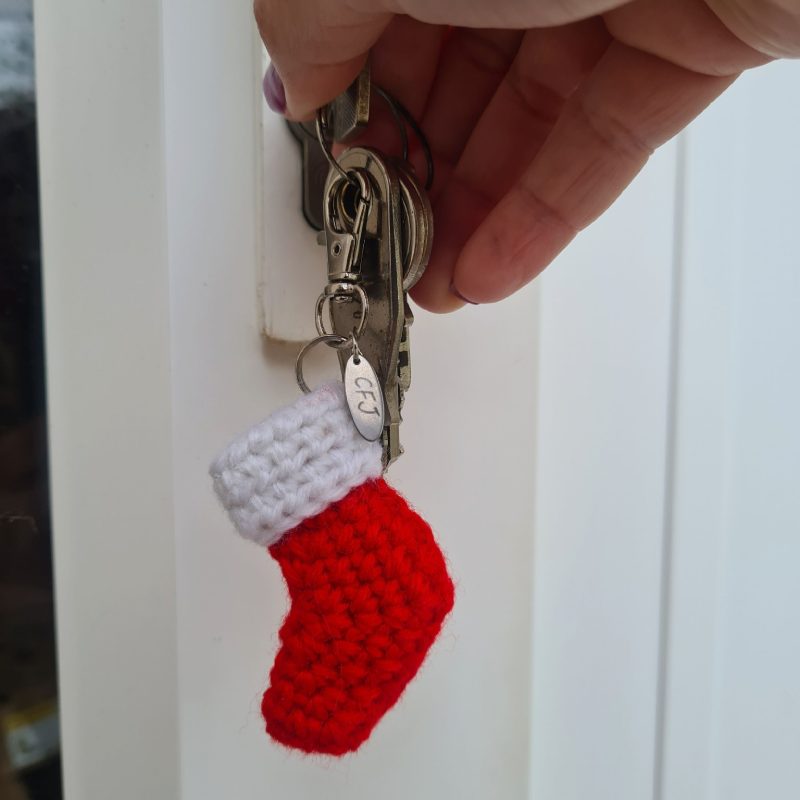 Red and white crochet Christmas stocking keyring attached to keys opening a door