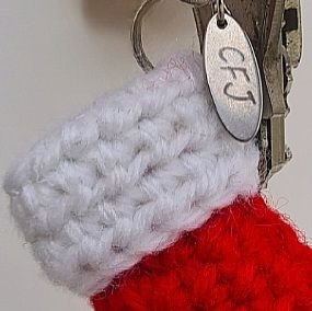 Close up of the top of a red and white crochet stocking keyring showing the stitch detail and logo
