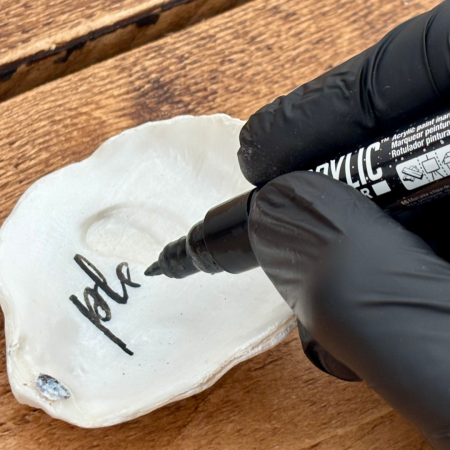 hand-lettering a message onto one of SHUCKED’s prepared oyster shells